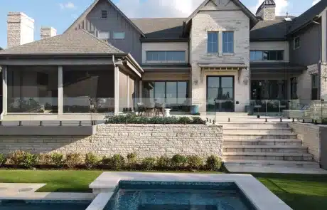 Back exterior of the home showing symmetrical windows, patio, glass railing, and stairs leading down toward the pool.